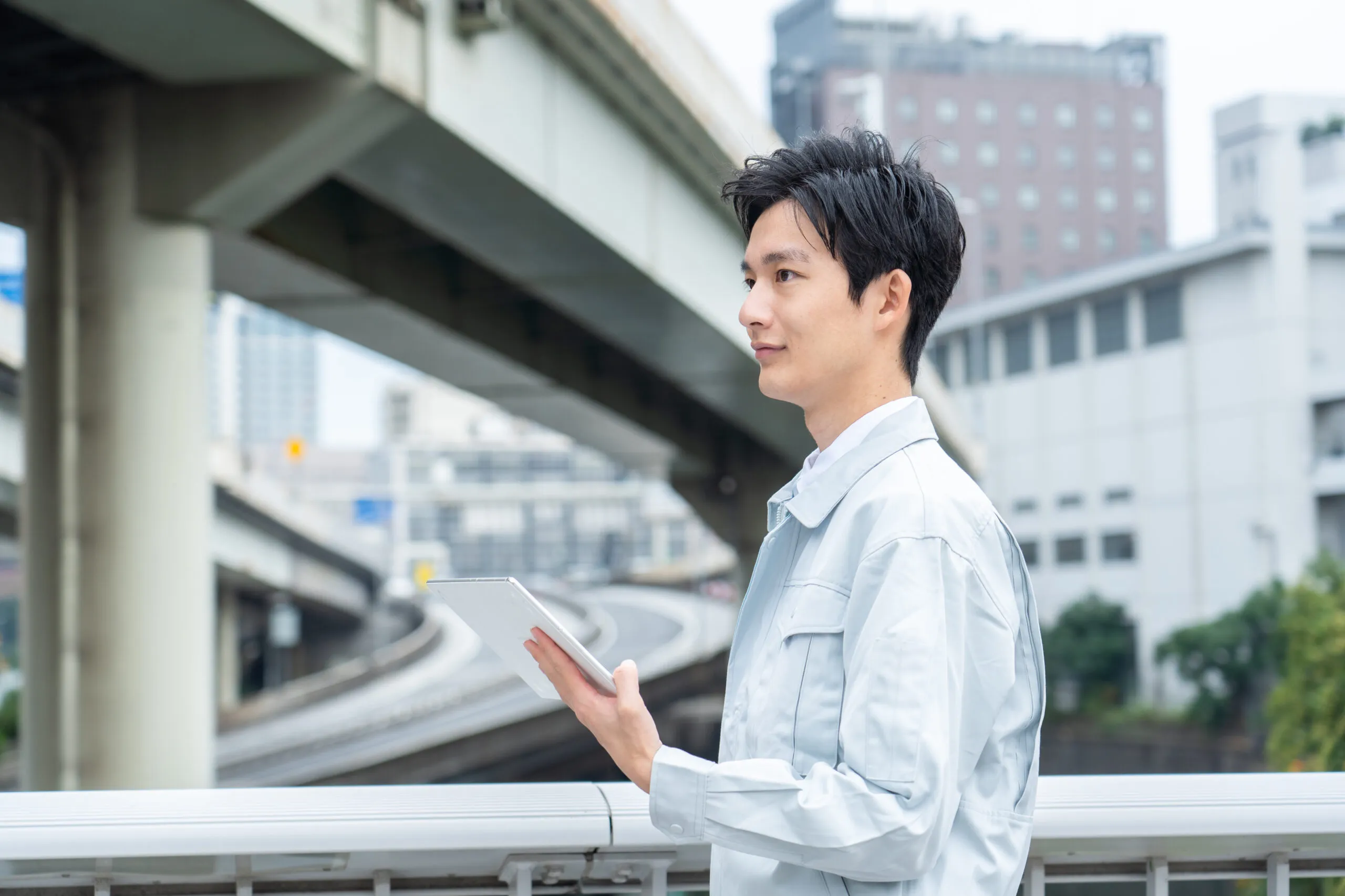 高架道路を背景にタブレットで現場を確認する技術者
