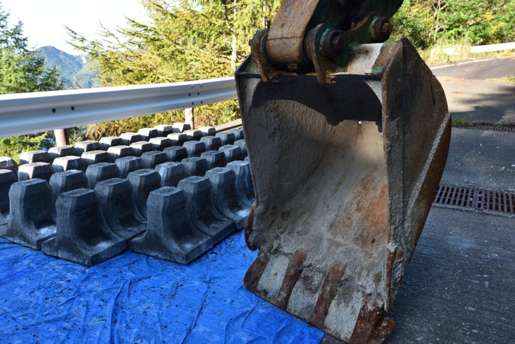 山間部の道路脇に積まれた擁壁ブロックと重機