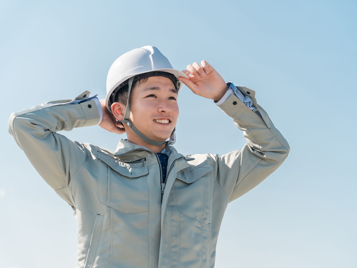 青空の下でヘルメットをかぶり直す若手の現場担当者